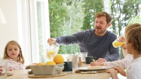 Father pouring orange juice as family wearing pyjamas sit around table enjoying pancake breakfast together - shot in slow motion - Powered by Shutterstock - Get 15% off with code: PIKWIZARD15
