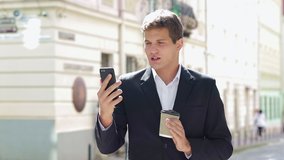Young attractive businessman standing on the street drinking coffee and using phone near business center.