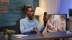 African lady having virtual meeting using phone sitting at desk in living room workplace. Black freelancer working with remotely team chatting virtual online conference, using internet technology