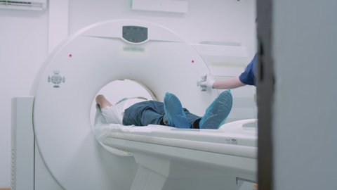 A patient in a medical mask is lying at a modern computer tomography machine. The doctor analyzes the lungs on a CT scanner. The danger of covid or coronavirus. Examining the organ of the lungs