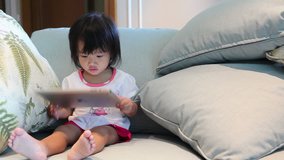 A little asian girl touching on wireless tablet and sitting on safa in the living room