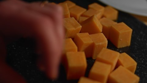 Cheddar cheese cubes being arranged on a wooden tray as tasty and attractive-looking appetizer. 4K video. Timelapse