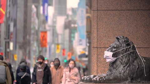 tokyo, japan - january 08 2021: Video of pedestrians wearing masks passing by the bronze sculpture of lion wearing a also a mask during the coronavirus pandemic at the Mitsukoshi store of Ginza.
