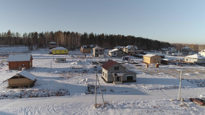 Aerial view of Houses under construction in winter cottage village. There are forests and fields around the village. There are free ground for construction
