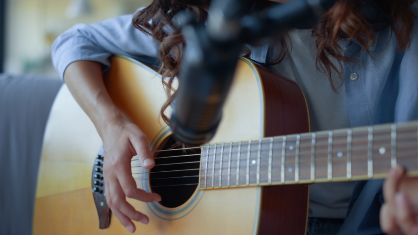 Teenage girl fingers strumming strings of guitar. Focused woman recording guitar sound with professional microphone. Female guitarist using condenser microphone at home. Young lady playing guitar