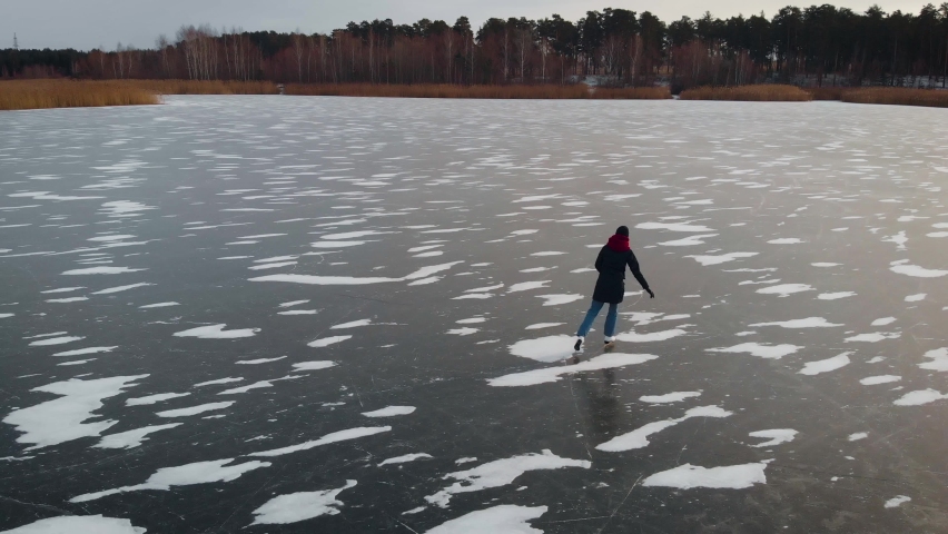 Aerial view. A young woman is skating on a frozen lake.