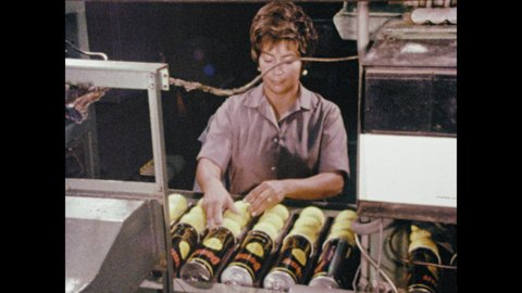 1970s: Factory, tennis balls fall into bin, travel down conveyor belt, woman inspects for quality. Woman lines up balls, logo is printed, woman rolls balls into canister.