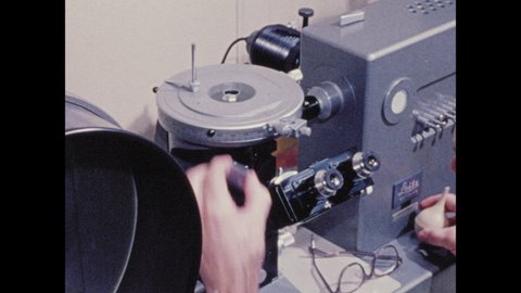 1970s: Man in white lab coat sits and looks into eyepiece of machine. Man adjusts the equipment. Dots and streaks inside of viewer.