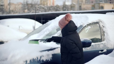 Female Cleaning Fresh Snow After Snowstorm From Vehicle.Sweep Snow From Automobile With Brushes In Winter.Scraping Ice From Glass.Woman Cleaning Car After Snowfall.Brushing Snow And Ice From Car Glass