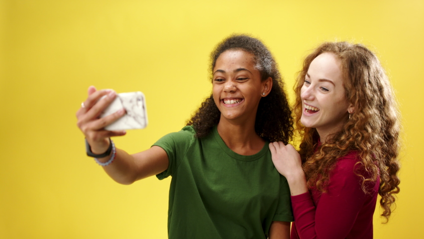 Young woman with teenager girl in a studio on yellow background, taking selfie.
