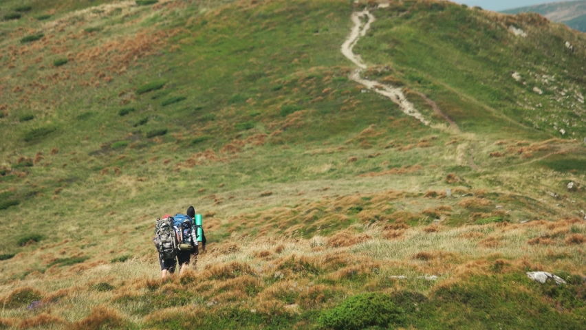 Tourists with hiking backpacks in summer mountins. Three hikers in mountains on a sunny day. Active leisure and tourism concept.