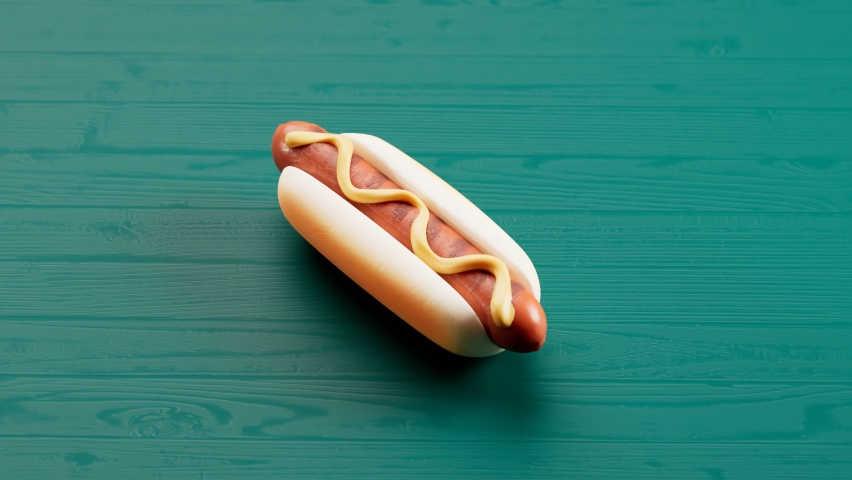Cheerful animation of eating fast food. Delicious hot dog despairing piece by piece. Buns with sausage and mustard at the green table. Tasty high fat snack. Junk food. Seamless looping footage. 4K HD Royalty-Free Stock Footage #1065848695