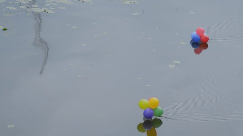 Colorful helium balloons floating in polluted river. Environmental protection, ecology, water pollution and garbage concept