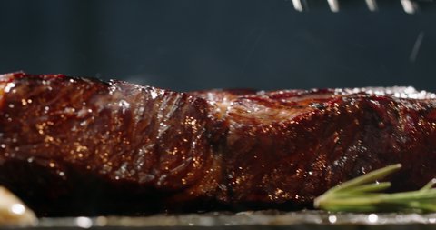 Close up shot of piece of steak is fried on the grill pan. Chef flips tasty grilled meat steak in kitchen, 4k footage