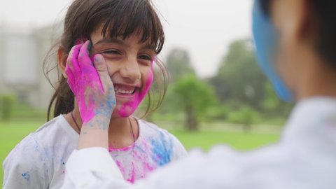 close view shot of young adorable kids applying colors on each other's face during Holi fest where a cute little girl is laughing and enjoying the moment.