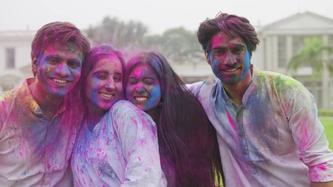 Close front view shot of a young group of male and female Indian close friends smeared or covered with colors smiling and laughing together looking at the camera during cultural Hindu fest of Holi