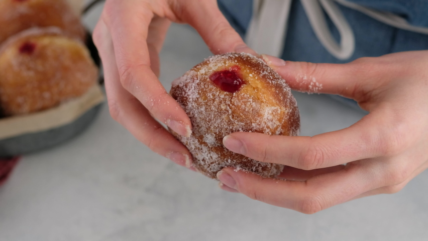 Berliners. Close-up female hands breaking a donut with raspberry jam on a white background, a cutaway donut with a filling filling. Delicious sweet donut. Making donuts with jam. Royalty-Free Stock Footage #1065861850