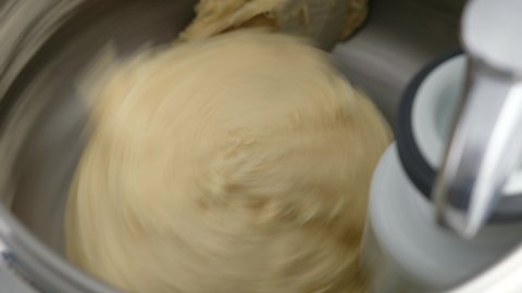 Machine kneading dough for donuts. Preparation of raw dough from butter, flour, sugar, milk, eggs and yeast in a dough mixer for industrial bakeries. Making homemade donuts. Close-up