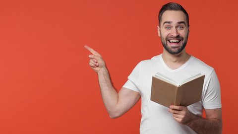 Excited cheerful bearded young man 20s in white casual t-shirt isolated on orange color background studio. People sincere emotions lifestyle concept. Reading book say wow pointing index finger aside