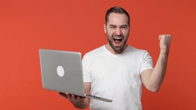 Excited happy bearded young man 20s in white casual t-shirt isolated on orange color background studio. People lifestyle concept. Working on laptop pc computer doing winner gesture screaming say yes - Powered by Shutterstock - Get 15% off with code: PIKWIZARD15