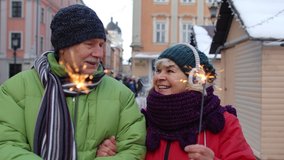 Senior couple with burning sparklers celebrating anniversary on winter city center street. Elderly family holding bengal lights enjoying Christmas eve. Active retired pensioners celebrating birthday - Powered by Shutterstock - Get 15% off with code: PIKWIZARD15