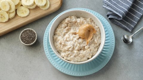 Oatmeal porridge with peanut butter. Woman's hands adding spoon of creamy peanut butter into breakfast oats. Healthy food, clean eating, dieting concept