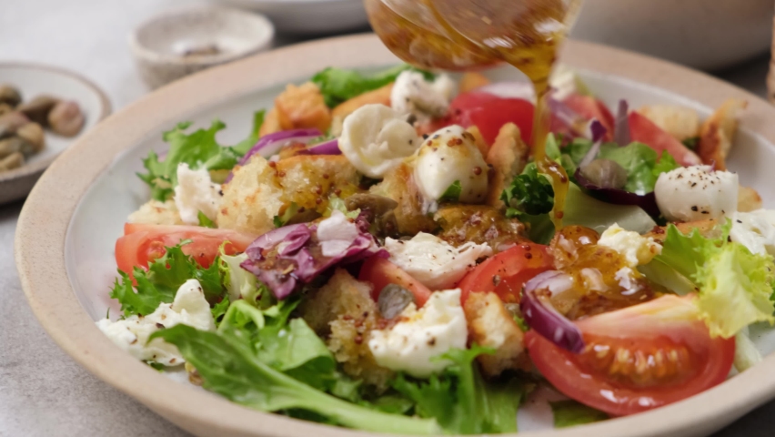 Pouring salad with honey mustard olive oil dressing. Healthy italian salad with tomatoes, mozzarella cheese, croutons, greens, capers and purple onion Royalty-Free Stock Footage #1065879751