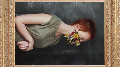 Vertical mirror reflection of young redheaded woman in marsala face mask decorated with meadow flowers turning to camera and posing against black studio background.