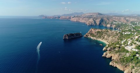 Aerial view above the Mediterranean Sea, with boat sailing in the water next to town on the edge of a cliff 4K