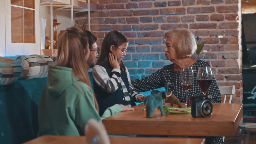 Happy grandmother giving amazing gift. Happy beautiful young girl celebrating birthday receiving presents her parents. Grandmother hugging her granddaughter while spending party holiday in cafeteria | Shutterstock HD Video #1065893728