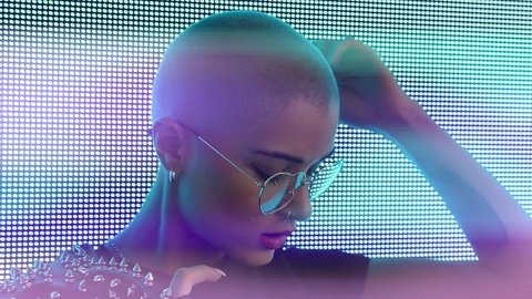 Cinematic video of a beautiful young woman posing against a led panel. Teenager with alternative futuristic cyberpunk look dancing and having fun into light streams. 
