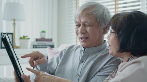 Candid old asian retired couple use tablet computer to transfer money online or financial payment and read text, smile or laugh with happy and positive. Senior asia with digital technology concept.