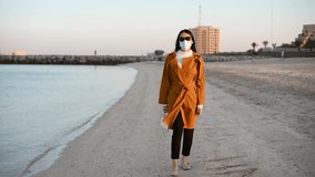 Woman walking by the seaside wearing surgical face mask during covid 19 pandemic. Walk to clear your mind and relax
