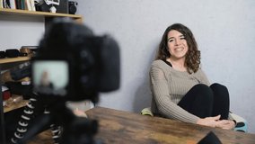 Young smiling woman sitting at the desk talking to the camera while taking a shot. Vlog and freelancer concept.