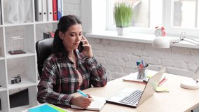Slow motion portrait of curly beautiful smiling female working. Attractive girl in office. Young business woman in office speak on the phone look at the window and making notes.