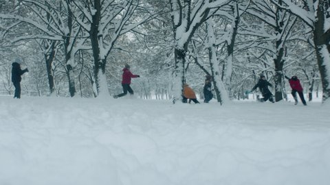 HANDHELD Diverse group of kids having snowball fight brawl, running through the park trees covered with snow. Fun winter games outside. 120 FPS slow motion shot