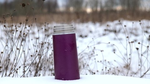 Small thermos with steaming hot drink on snowy winter background