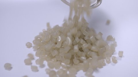 Secondary white granules of recycled plastic are poured out of the vessel onto a white sheet. Polymer granules are used for the production of plastic products.