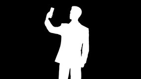 Silhouette of man using phone to take selfie against black background