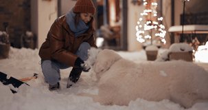 Young woman playing with her white dog, throwing a snow, having fun on the backyard during winter holidays. Slow motion video