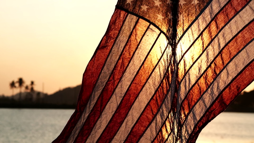 American flag waving on sunset or sunrise background with soft focus, Slow Motion. Concept of Memorial Day or 4th of July, Independence Day, Veterans Day, American Election, National Celebration. Royalty-Free Stock Footage #1065913525