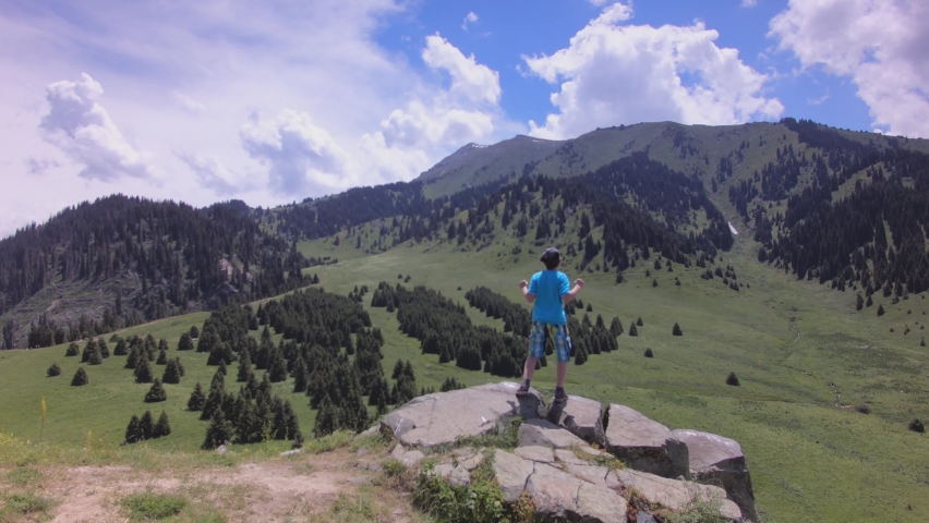 Teenage boy jumps on the rock and looks at the mountain plateau from above. Far at the distance mountain ridge