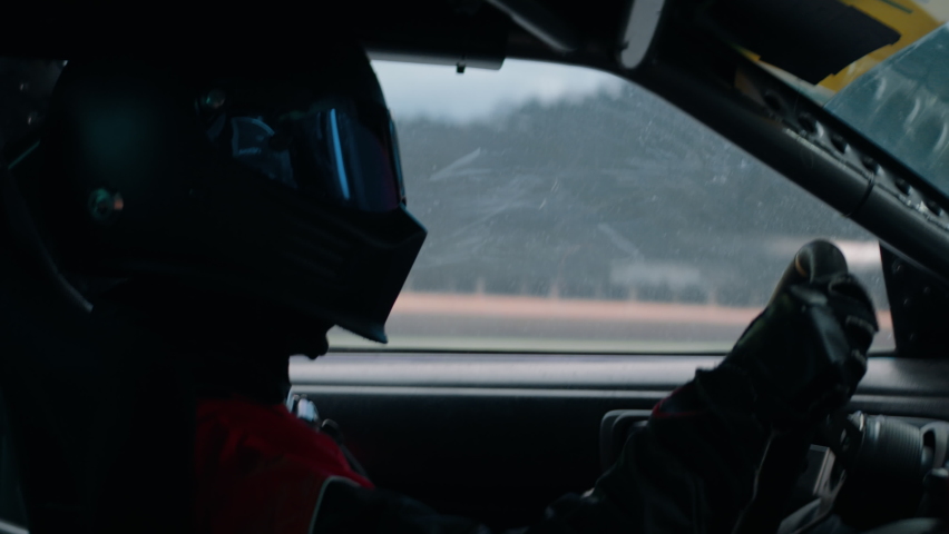 CU View of unrecognizable driver in protective wear driving a sports car, racing on a speedway. Shot with 2x anamorphic lens