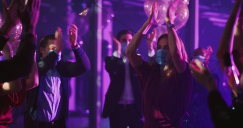 Group of happy young millennial people dancing together at night club. Formally dressed diverse colleagues wearing face masks celebrating corporate party.