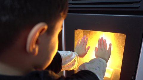 4K Boy warms up his hands against the fire in furnace
