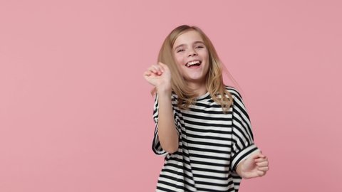Cheerful little kid girl 12-13 in striped t-shirt isolated on pink background studio. Childhood lifestyle concept. Dancing doing dab hip hop dance hands move gesture youth sign hiding covering face