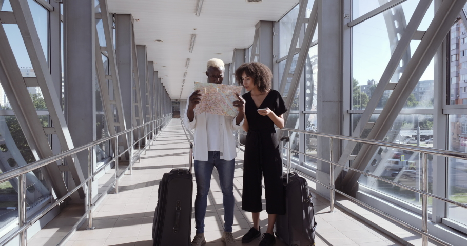 Afro american couple young family on their honeymoon two friends man and woman stand in airport terminal looking for right way point hotel looks at map and into mobile phone quarreling angry arguing. Royalty-Free Stock Footage #1065931384
