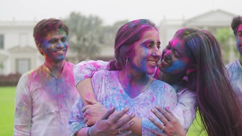 Close front view shot of a young group of male and female Indian close friends smeared or covered with colors hugging, smiling and laughing together looking at the camera during Hindu fest Holi