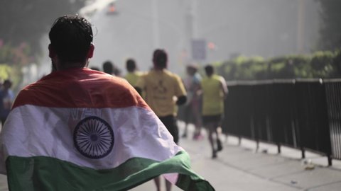 Back shot of a young runner carrying an Indian national flag or Tricolor on his back wrapped around his shoulders running along with other runners in an ultra marathon, Mumbai, India 