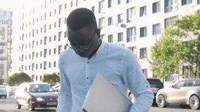 Portrait of young serious successful black businessman person worker holding silver laptop looking at camera on the street, ready to go for a job